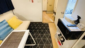 Ett kompakt hotellrum med en säng, ett litet skrivbord med en dator och en väckarklocka, en mikrovågsugn och ett fönster med utsikt över gatan.