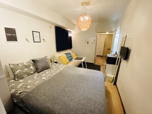 A compact hotel room with a bed, a small desk, a television, and a kitchenette. - Best Apartment in Shinjuku (Tokyo)
