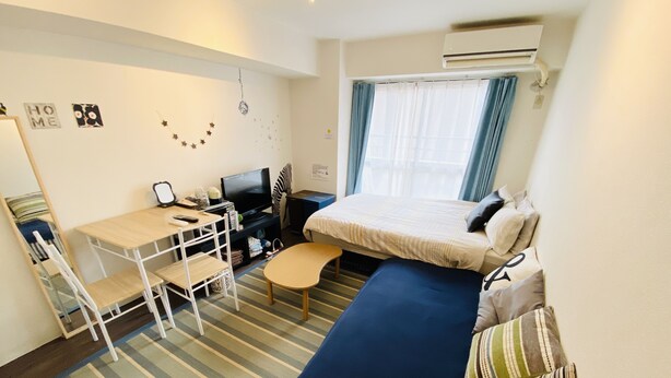 Ett kompakt hotellrum med en säng, ett skrivbord med en dator, en stol, ett litet bord och en randig matta.