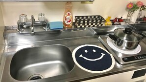 Une cuisine avec un évier en acier inoxydable, un tapis orné d’un visage souriant, une bouteille de liquide vaisselle et un panier à carreaux.