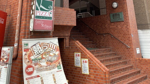 Un bâtiment en briques avec une enseigne indiquant un restaurant de pizzas, un escalier et un balcon.