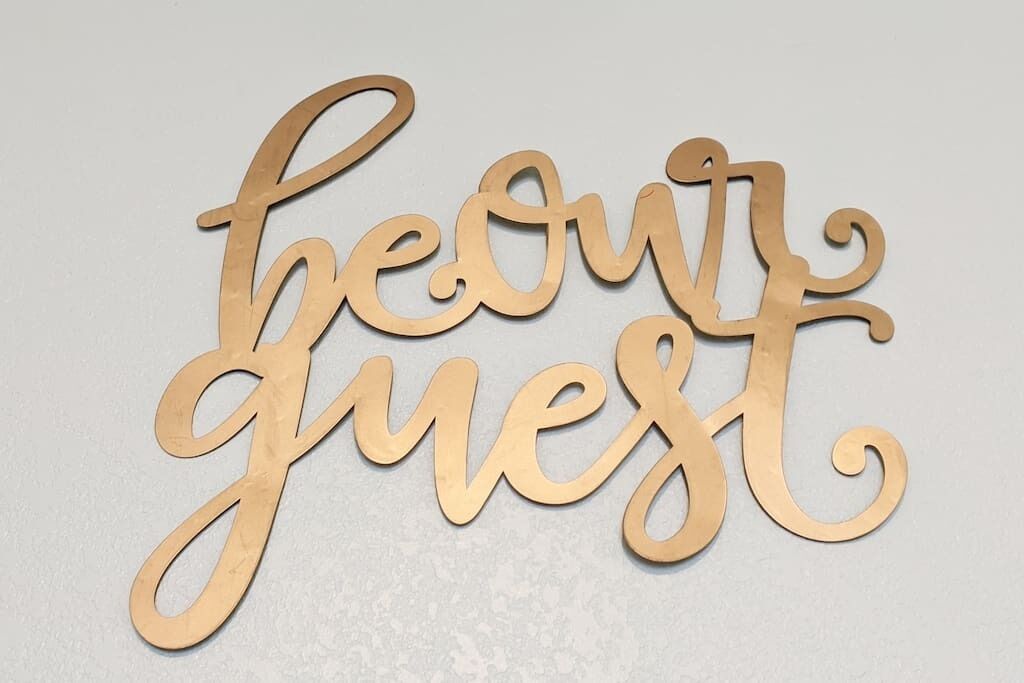 A wooden sign with the words "be our guest" in cursive lettering.