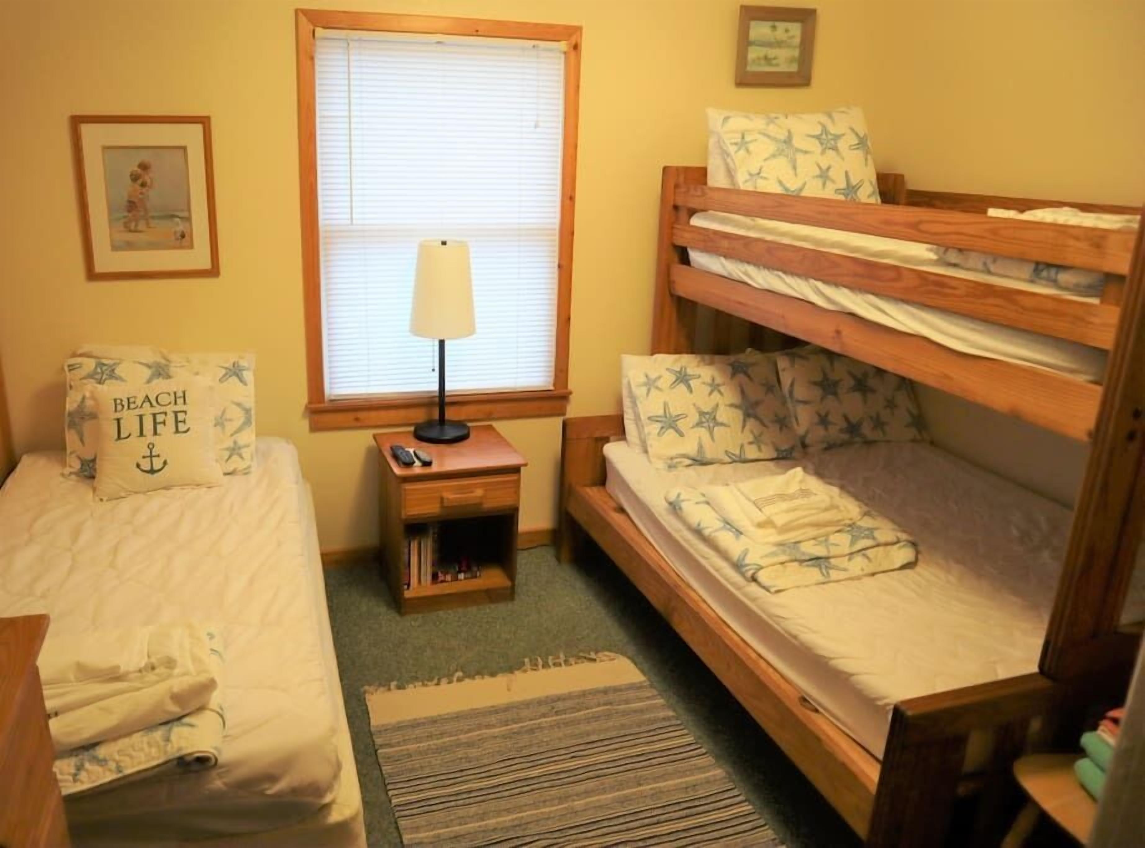A room with a bunk bed, a bedside table with a lamp, and a small nightstand with books.