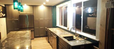 A modern kitchen with a marble countertop, stainless steel appliances, and a large window providing natural light.