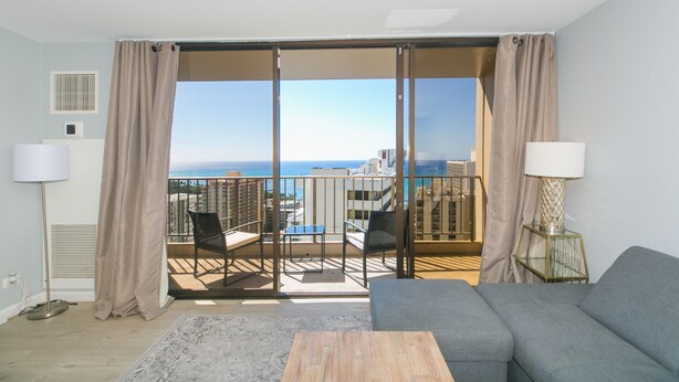 Un salon moderne avec un canapé, une table basse et un balcon offrant une vue sur la ville et l’océan.