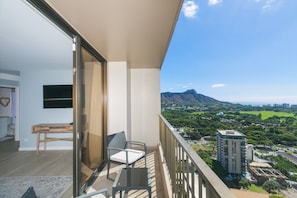 A balcony with a wooden table and a chair, overlooking a cityscape with mountains and greenery.