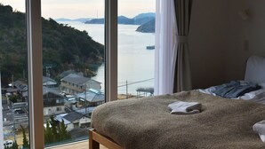 Une chambre avec une grande fenêtre donnant sur la côte, un lit avec une couverture et un oreiller.