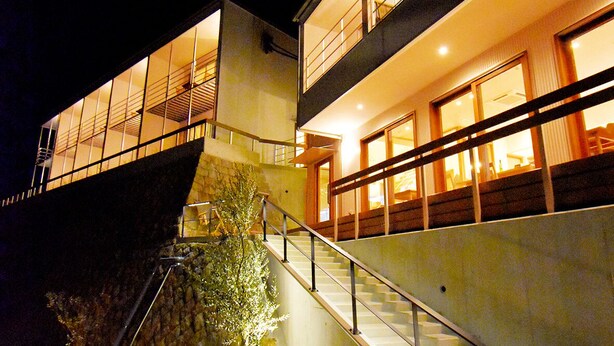 Un bâtiment moderne doté d’un escalier menant à un deuxième étage, entouré d’un espace paysager agrémenté d’un petit arbre et d’un rocher.