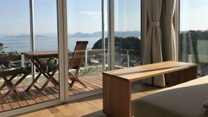 Un balcon avec une table et des chaises en bois, un banc et une vue sur la mer et les montagnes.