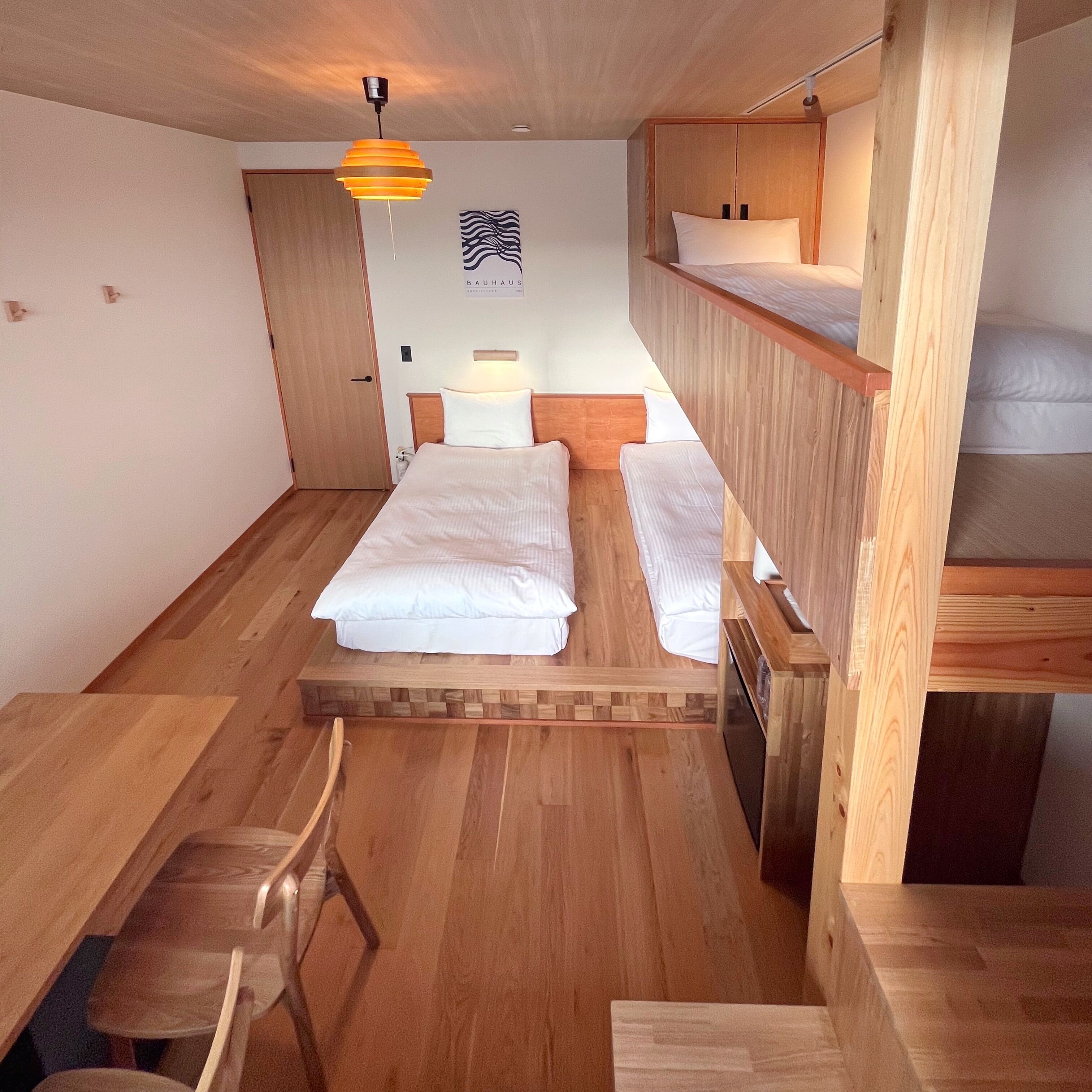 Una habitación pequeña con una litera, una cama individual, un escritorio de madera y una silla.