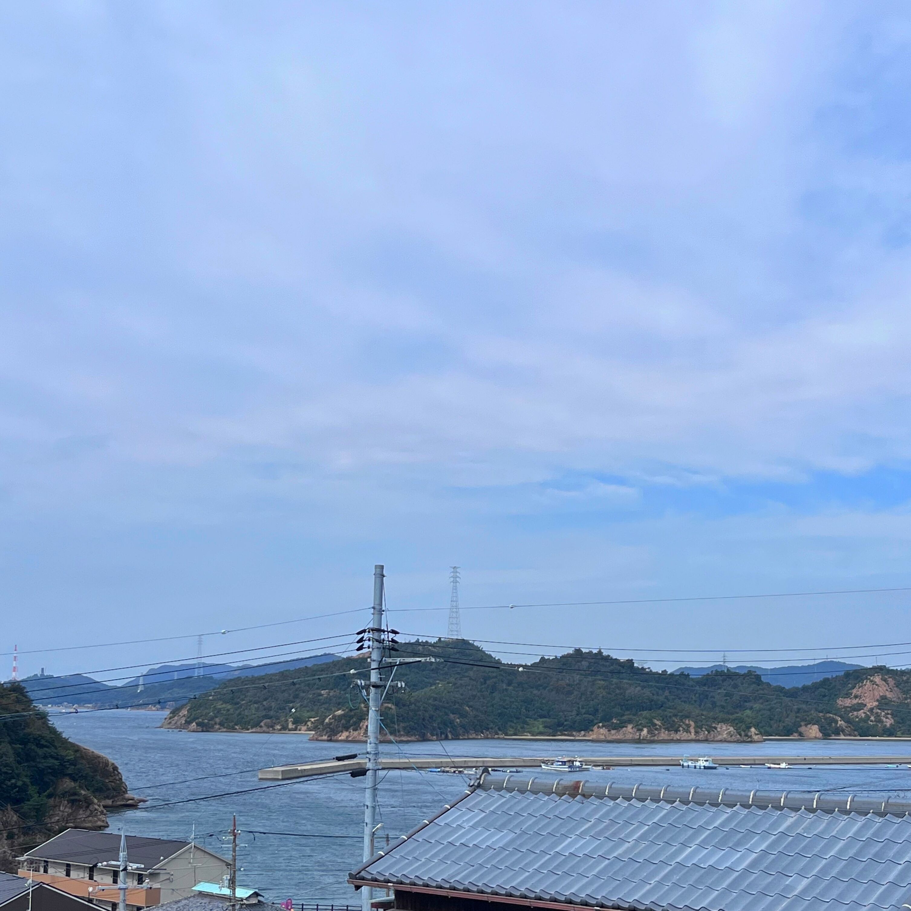 A coastal area with a view of the sea, a power line tower, and a distant mountain range.