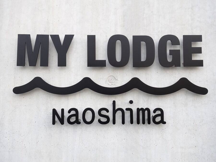 A sign with the text "MY LODGE" and "naoshima" on a textured wall.