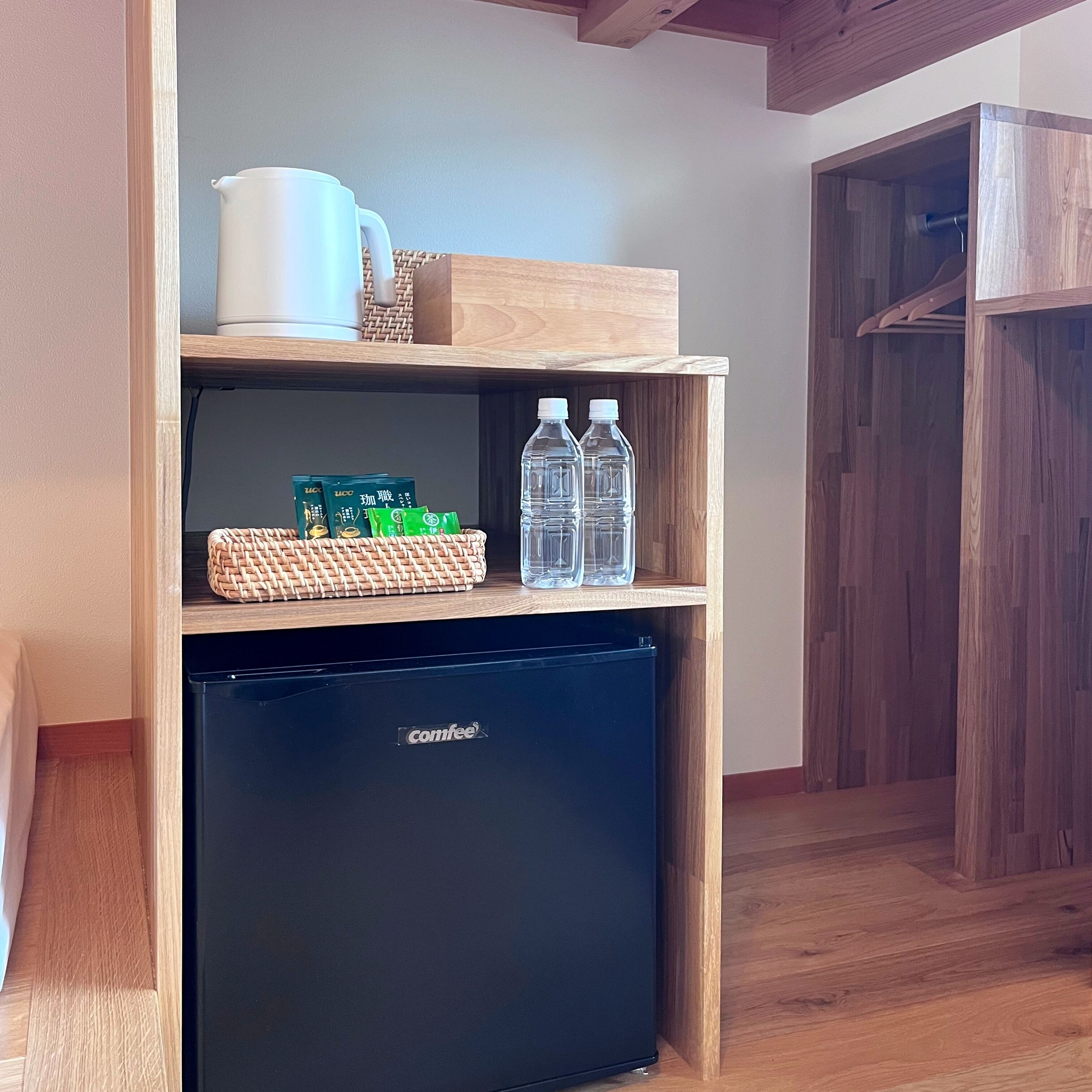 Una kitchenette compacta con un refrigerador negro Comfee, una cesta tejida y una repisa con agua embotellada y una taza blanca.