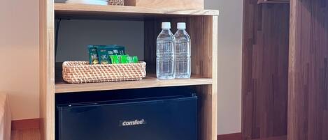 Una kitchenette compacta con un refrigerador negro Comfee, una cesta tejida y una repisa con agua embotellada y una taza blanca.