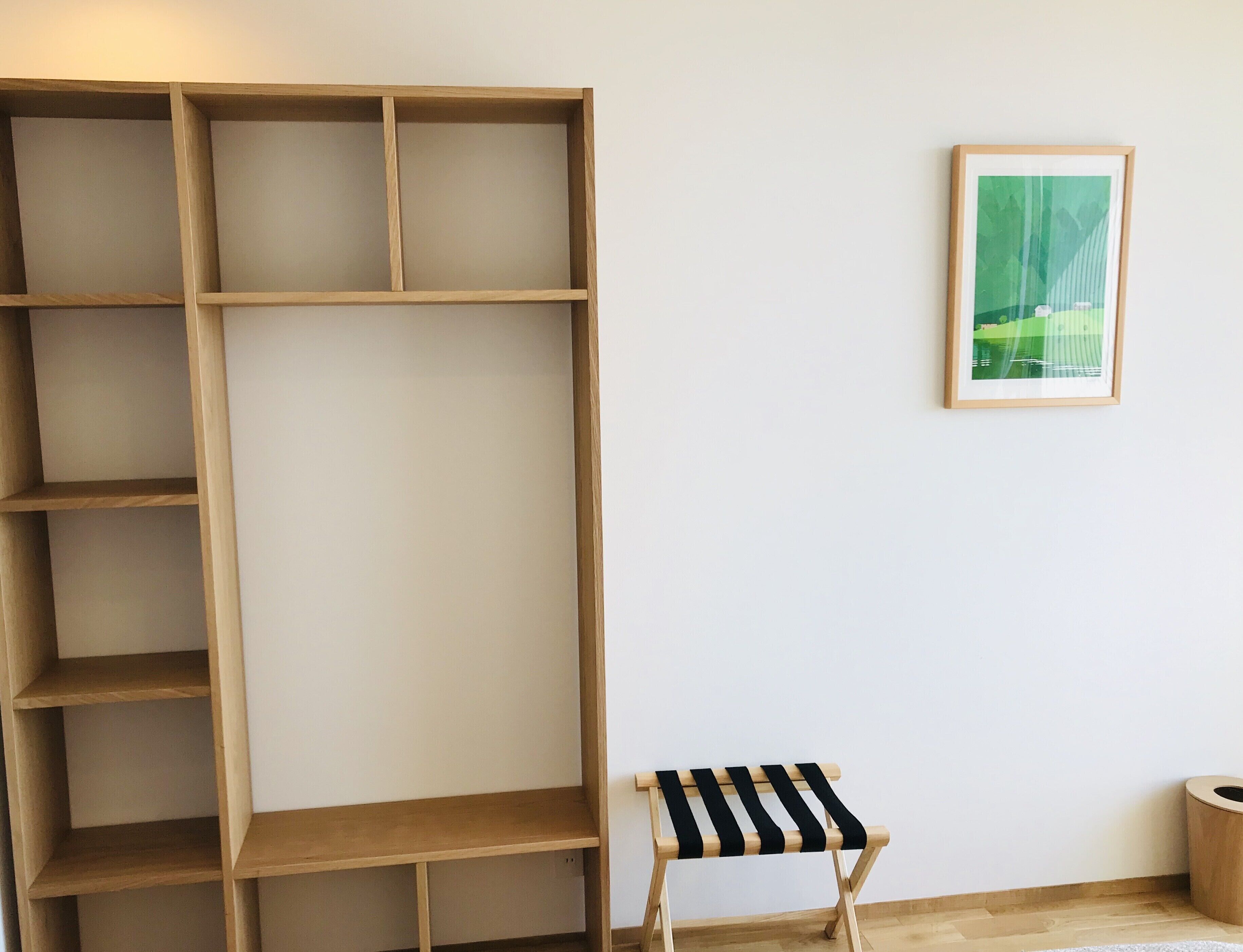 A room with a wooden bookshelf, a small black and white striped bench, and a framed picture on the wall.