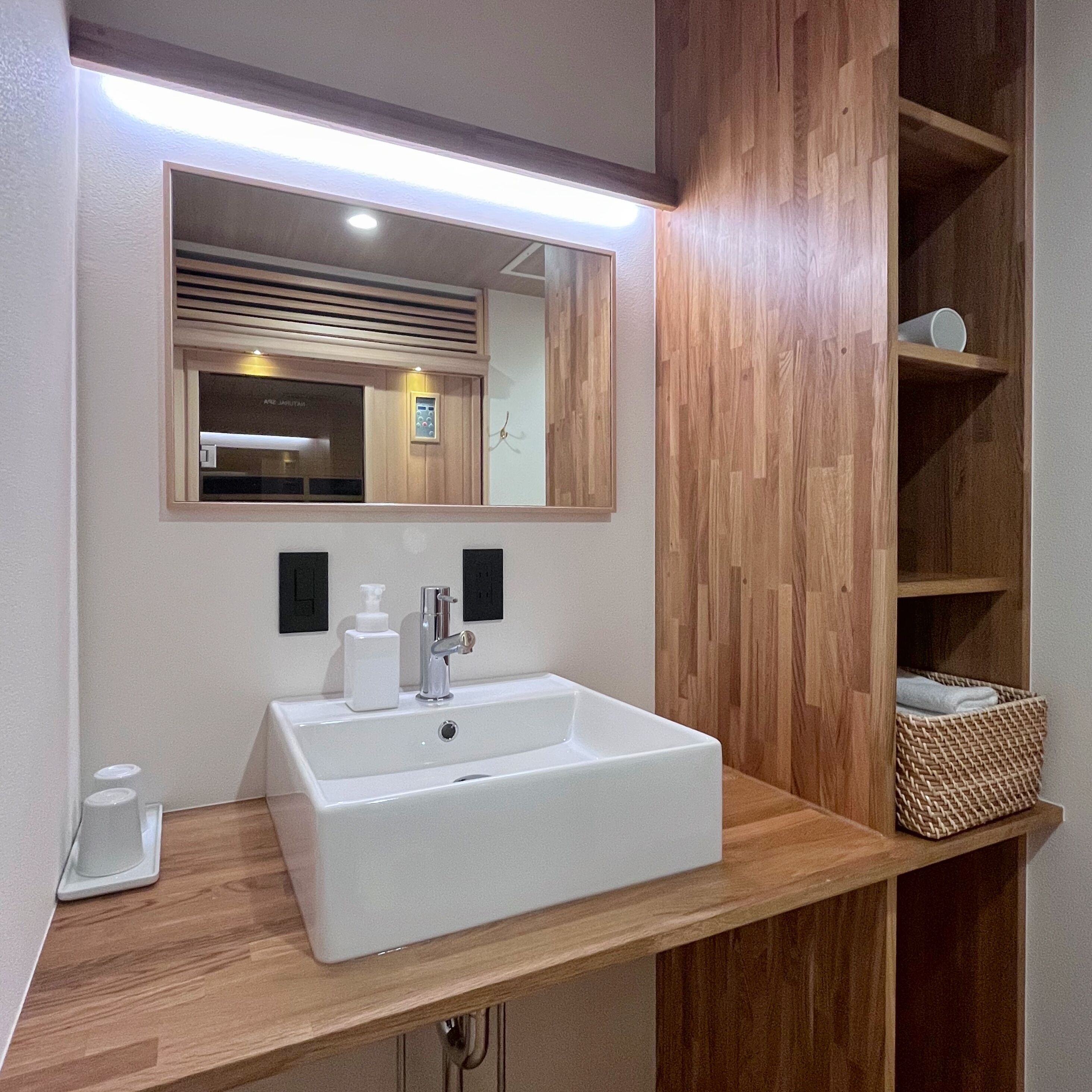 A bathroom with a white sink, a mirror, and wooden shelving.