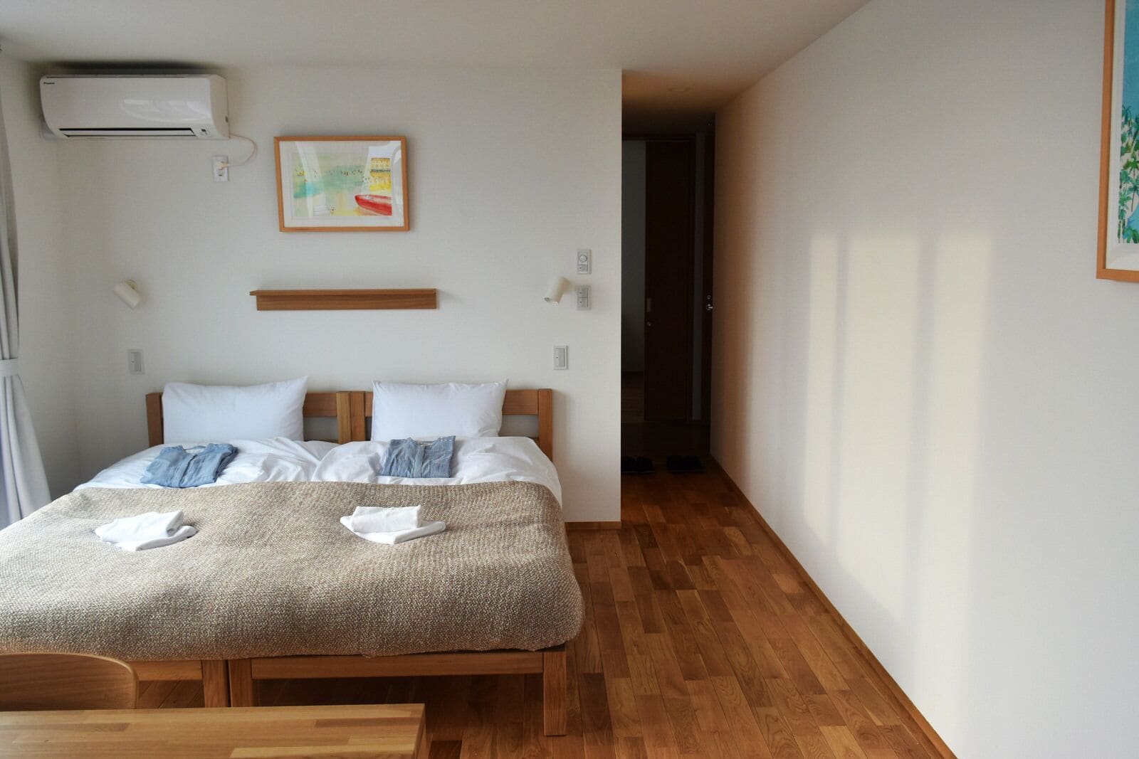 A neatly made bed with a blanket and towels, a wooden headboard, a wall-mounted air conditioner, and a framed picture.