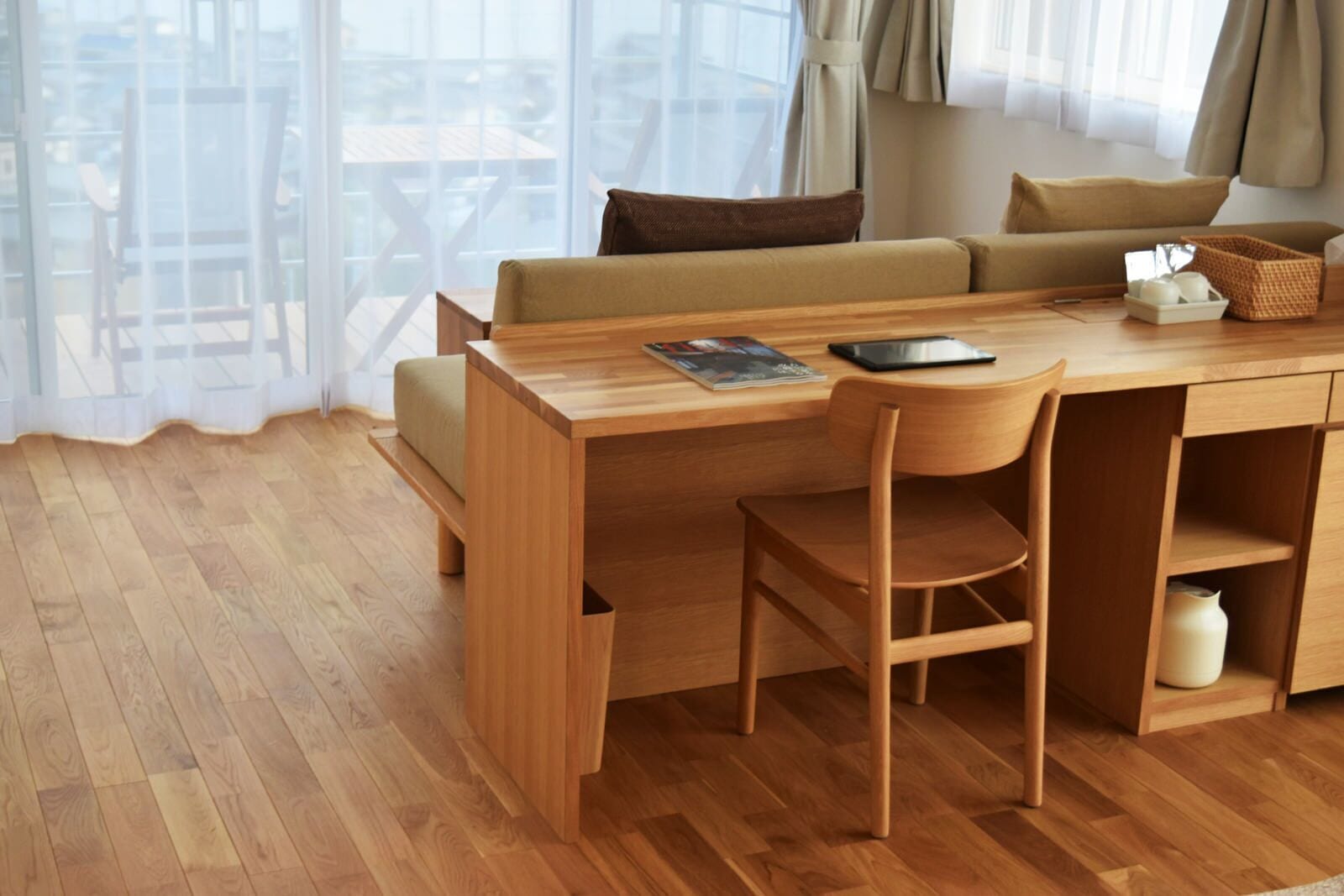 Een moderne, goed verlichte kamer met een houten bureau, een comfortabele bank en uitzicht door grote ramen.
