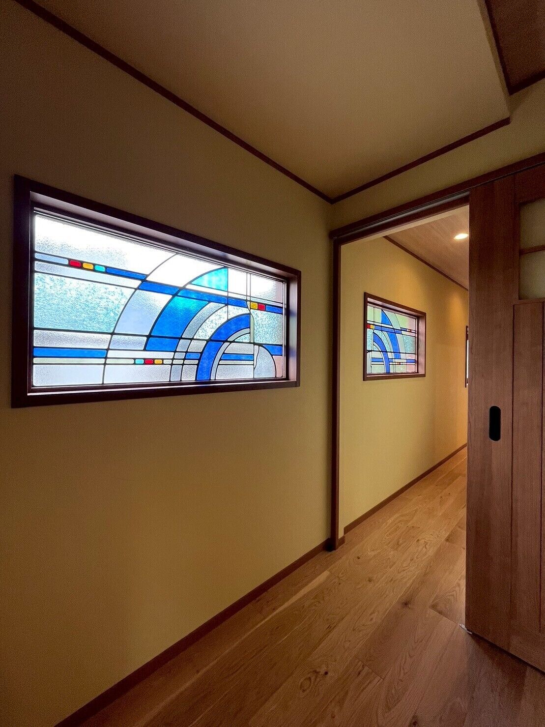 A hallway with wooden flooring and two large stained glass windows with blue and white patterns.