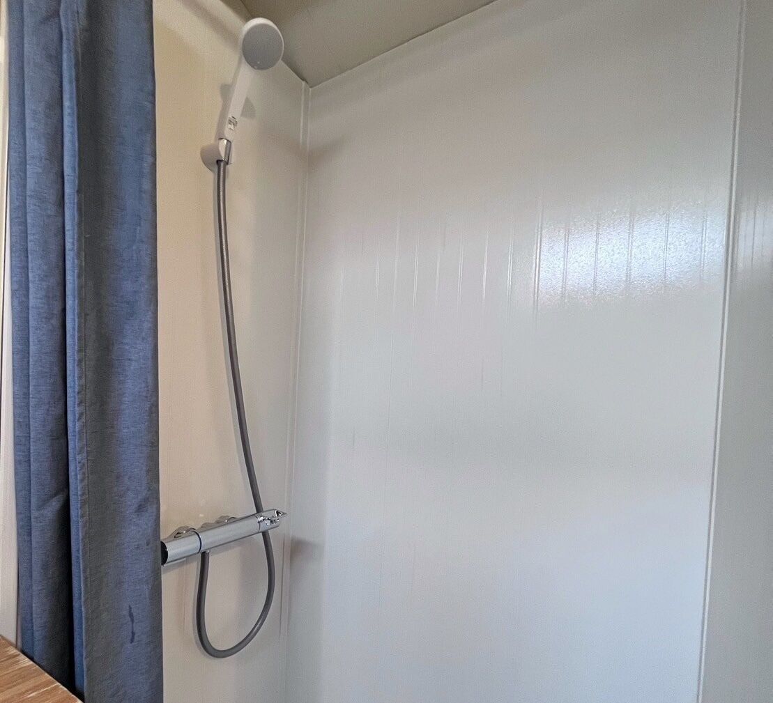 A shower with a handheld hose and a wall-mounted showerhead in a bathroom with white walls.