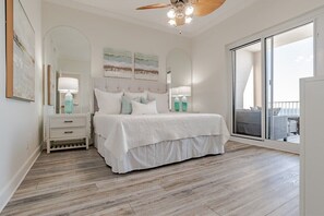 Relax in this serene bedroom with a large bed, nightstands, and a ceiling fan, offering a peaceful retreat with a balcony and outdoor seating.