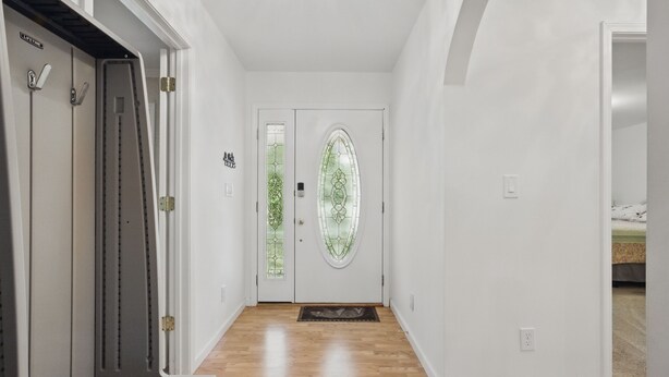 Un pasillo con piso de madera, paredes blancas y una puerta doble con un panel de vidrio.