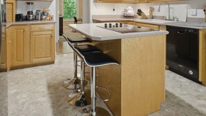 Una cocina moderna con armarios de madera, una isla central con taburetes de bar, lavavajillas y ventilador de techo.