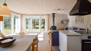 Une cuisine chaleureuse avec un plancher en bois, un coin repas avec une nappe à carreaux et une grande fenêtre donnant sur un jardin.