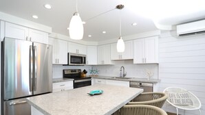 A modern kitchen with white cabinetry, stainless steel appliances, a granite countertop, and wicker chairs. - Oceanfront, Exceptionally Remodeled, Split A/C, King bed, OH the sunsets (Kihei)