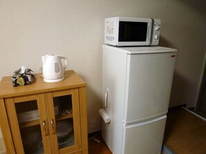 A white refrigerator with a microwave on top, a wooden cabinet with a glass door, and a white kettle on the cabinet.