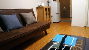 A living room with a brown sofa, a wooden cabinet, a white refrigerator, and a blue folder on a table. - Free bike & free WIFI 203 Take it easy (Kyoto)