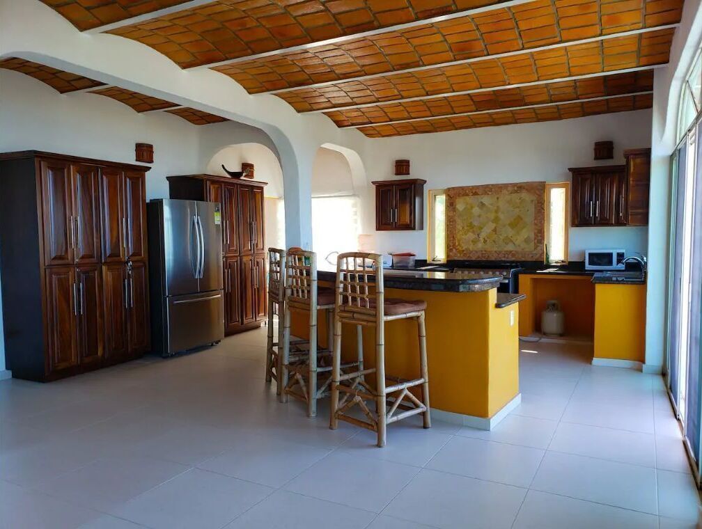 A spacious kitchen with wooden cabinets, a stainless steel refrigerator, and a central island with bar stools.
