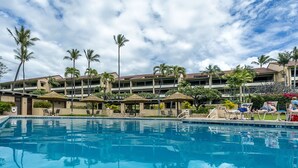Un hotel con piscina, palmeras y un edificio de varios pisos con balcones.