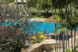 Un espace piscine avec une eau d’un bleu limpide, entouré de palmiers et agrémenté d’un parasol en chaume.