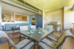 Un coin repas avec une table et des chaises en verre, une cuisine équipée d’un barbecue et un salon avec un canapé et une fenêtre.