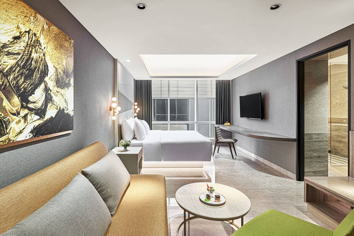 Une chambre d’hôtel moderne avec un grand lit, un canapé, une petite table avec un dessert, une télévision et un tableau au mur.