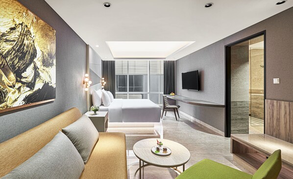 Une chambre d’hôtel moderne avec un grand lit, un canapé, une petite table avec un dessert, une télévision et un tableau au mur.