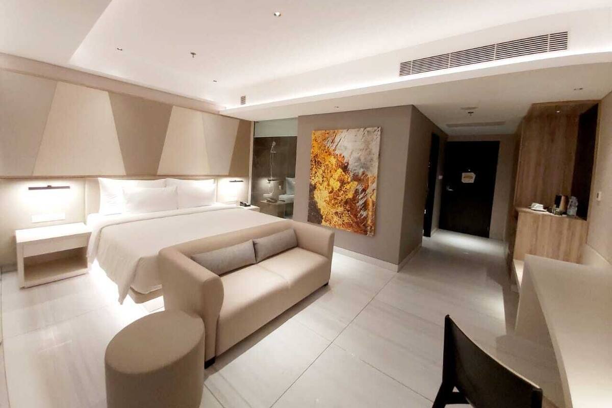 Une chambre moderne avec un lit, un canapé, un bureau et un grand tableau abstrait.