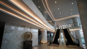 Un interior moderno con dos escaleras mecánicas, paredes de mármol y barandilla de vidrio.