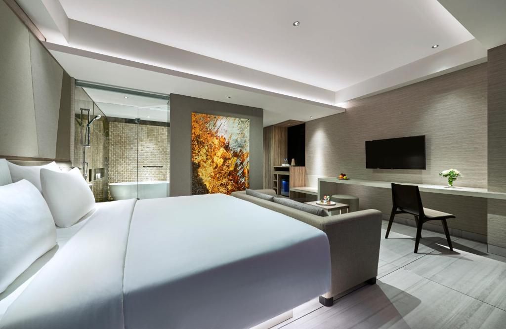 A modern hotel room with a large bed, a seating area, a flat-screen TV, and a shower area.