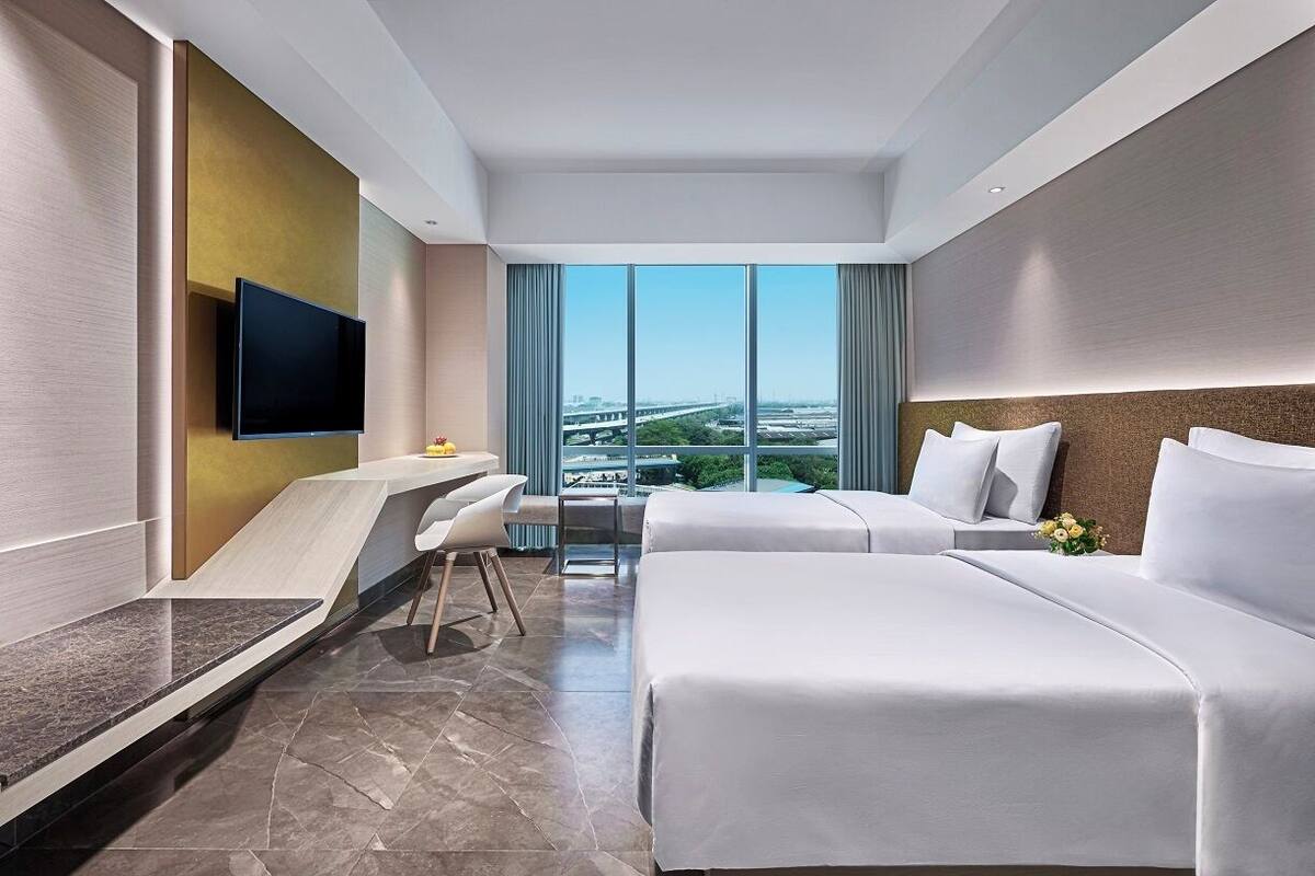 Une chambre d’hôtel moderne avec un grand lit, un bureau et un téléviseur fixé au mur.