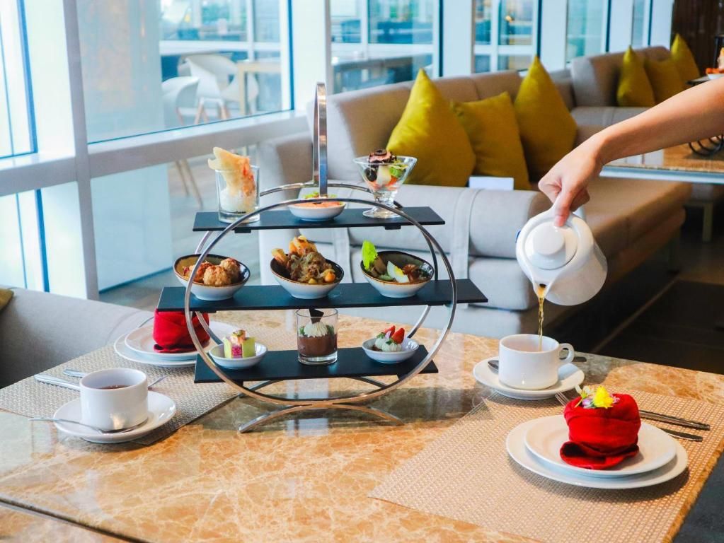 A three-tiered dessert stand with various sweets and a cup of tea on a table, with a sofa and a window in the background.