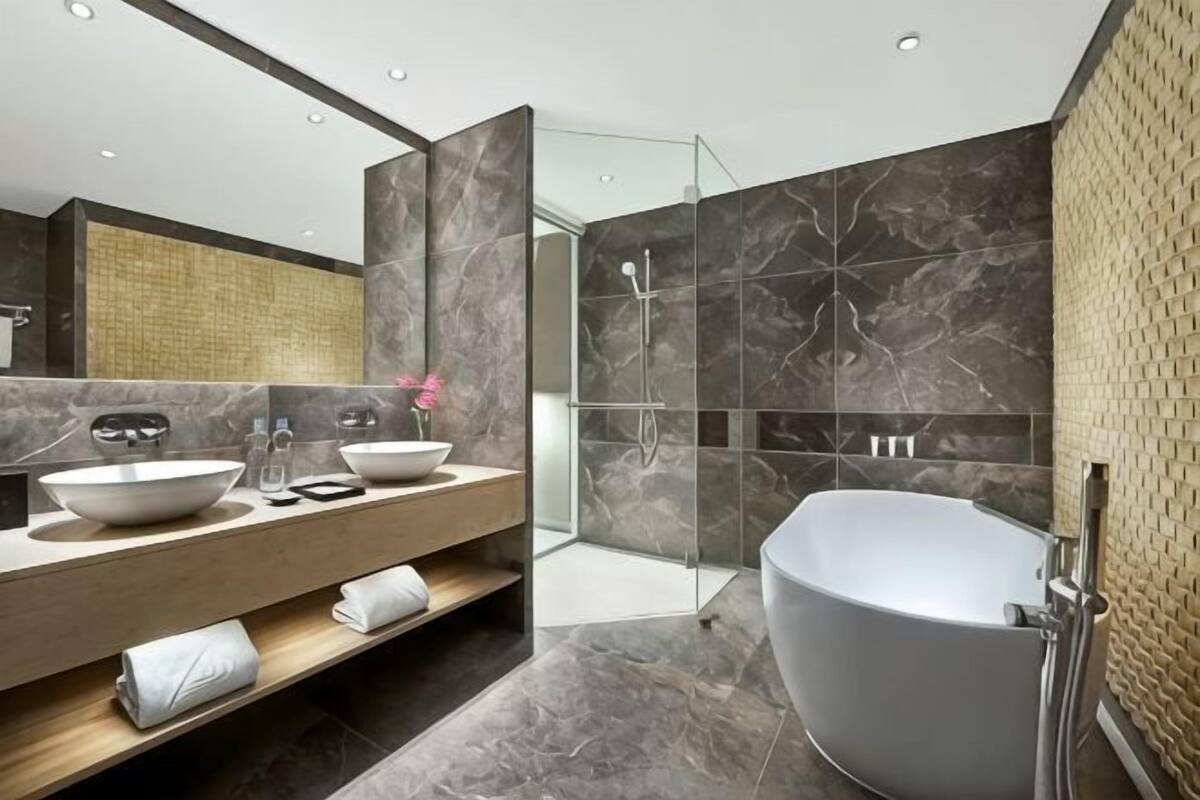 Une salle de bain moderne avec une baignoire sur pieds, deux vasques, une douche à l’italienne et un grand miroir.