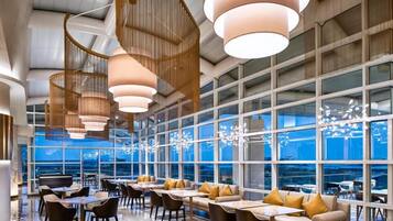 Un interior moderno con comedor, ventanas amplias y lámparas colgantes.