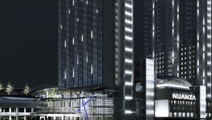 Un hotel moderno con un llamativo letrero 'NUANZA', que presenta un diseño vertical elegante con ventanas iluminadas y un atrio central.