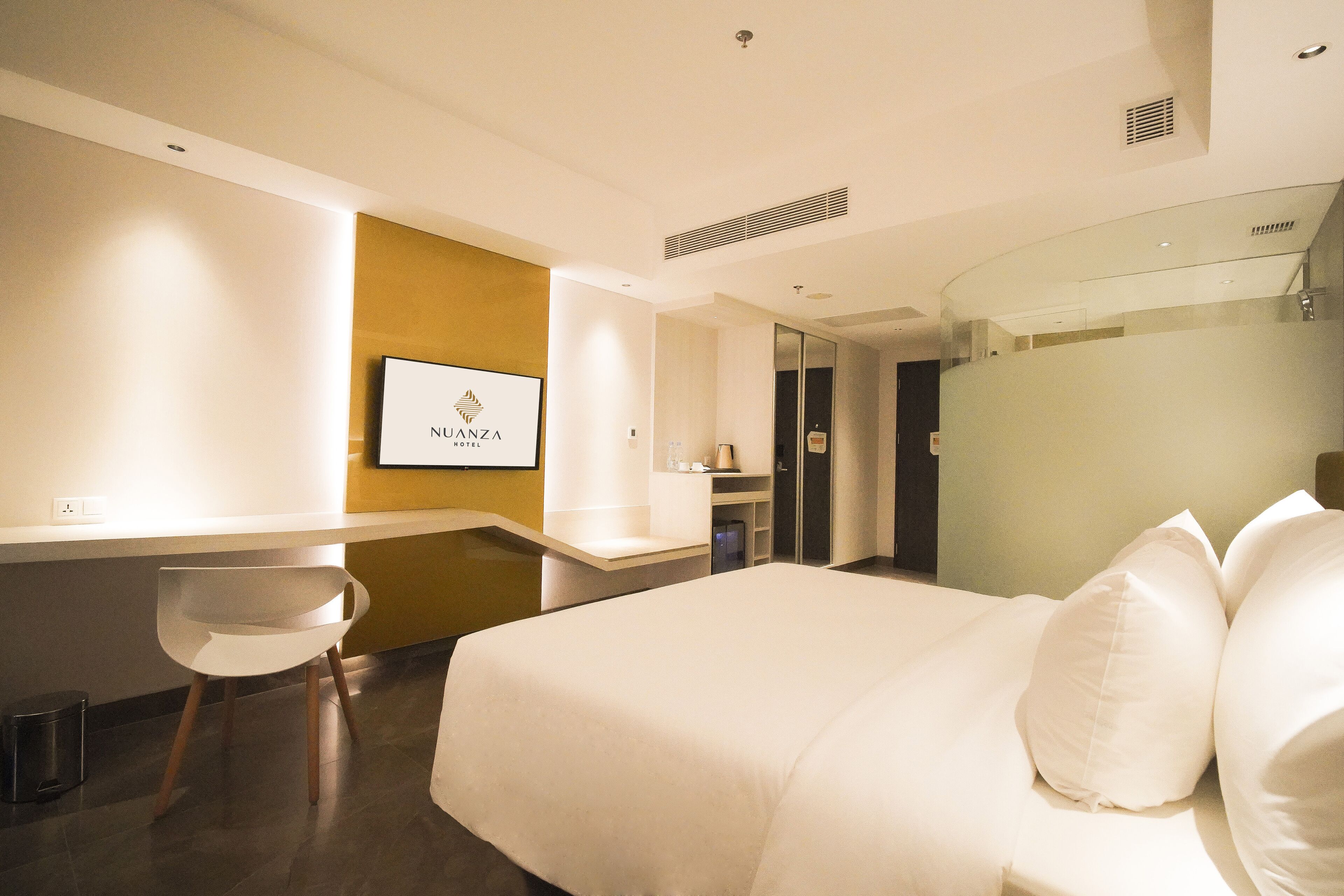 A hotel room with a bed, a desk, a chair, and a television displaying the hotel name.