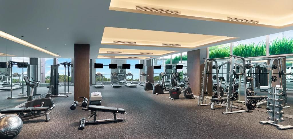Ein modernes Fitnessstudio mit verschiedenen Trainingsgeräten, großen Fenstern und Blick auf Grünflächen.