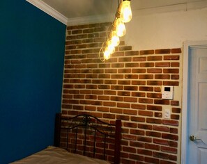 A room with a brick wall, a bed with a metal headboard, and a light fixture with multiple bulbs. - The standard apartment shibuya B (Tokyo)
