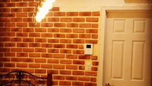 A room with a brick wall, a white door, a bed, and a thermostat on the wall. - The standard apartment shibuya B (Tokyo)