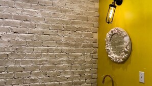 A bathroom with a brick wall, a yellow accent wall, a round mirror, and a white sink. - The standard apartment shibuya D (Tokyo)